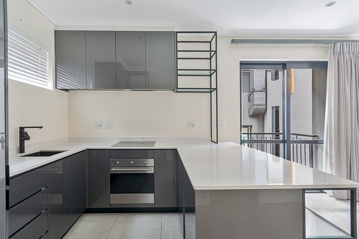 Modern kitchen featuring sleek grey gloss cabinetry, stone countertops, integrated oven and hob, and direct access to a private balcony.