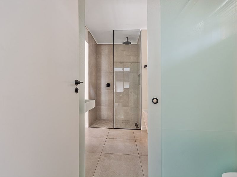 Modern bathroom featuring a walk-in shower with a glass screen, black fixtures, and neutral floor-to-ceiling tiling.