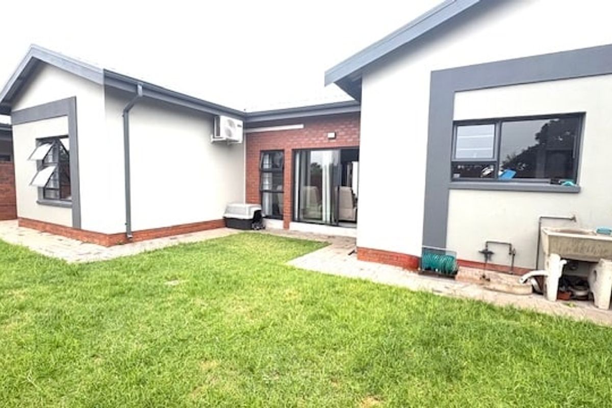 Rear view of the property featuring a paved patio area, a small lawn, and a functional exterior utility sink.