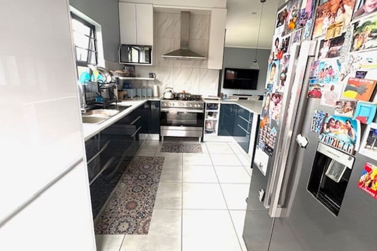 Modern kitchen featuring high-gloss cabinetry, stainless steel gas stove with extractor fan, tiled flooring, and a double sink.
