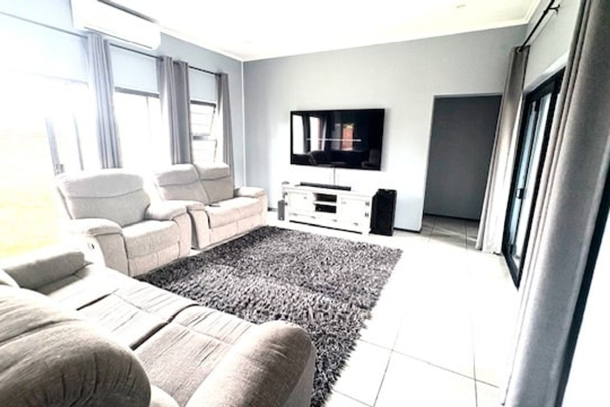 A bright and spacious living room featuring large windows, tiled flooring, and a wall-mounted television setup.
