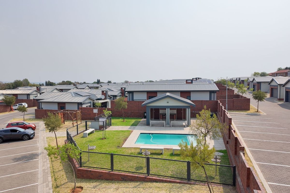Aerial view of a residential estate complex featuring a communal swimming pool, covered patio area, landscaped garden, and paved parking bays.