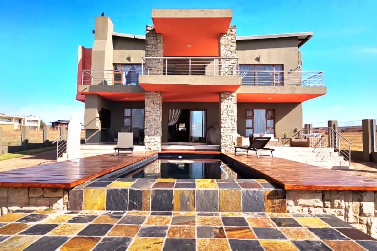 Rear elevation of a modern double-story house featuring a swimming pool, timber decking, stone-clad pillars, and a spacious upper-level balcony.
