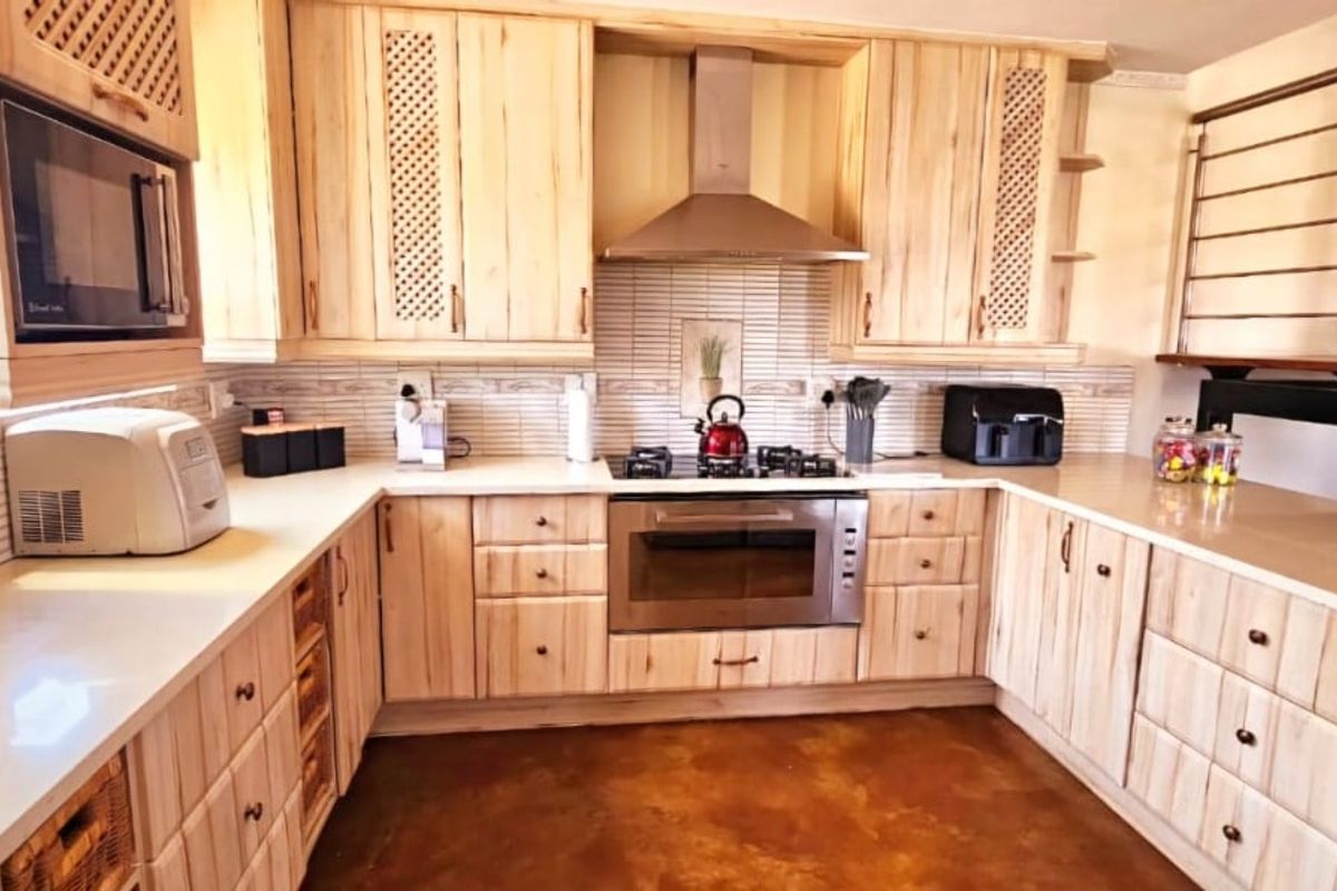 A well-appointed kitchen featuring light wood cabinetry, stone countertops, integrated stainless steel appliances, and a tiled backsplash, adjacent to an open staircase.