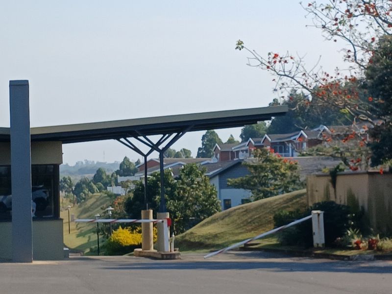 A view of the residential estate entrance featuring a security boom gate, guard house, and paved driveway leading into the complex.