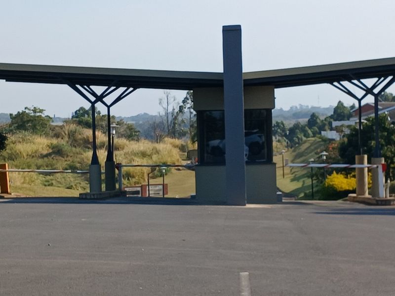 A view of the residential estate security gatehouse featuring a modern metal canopy, boom gate access control, and paved driveway entrance.
