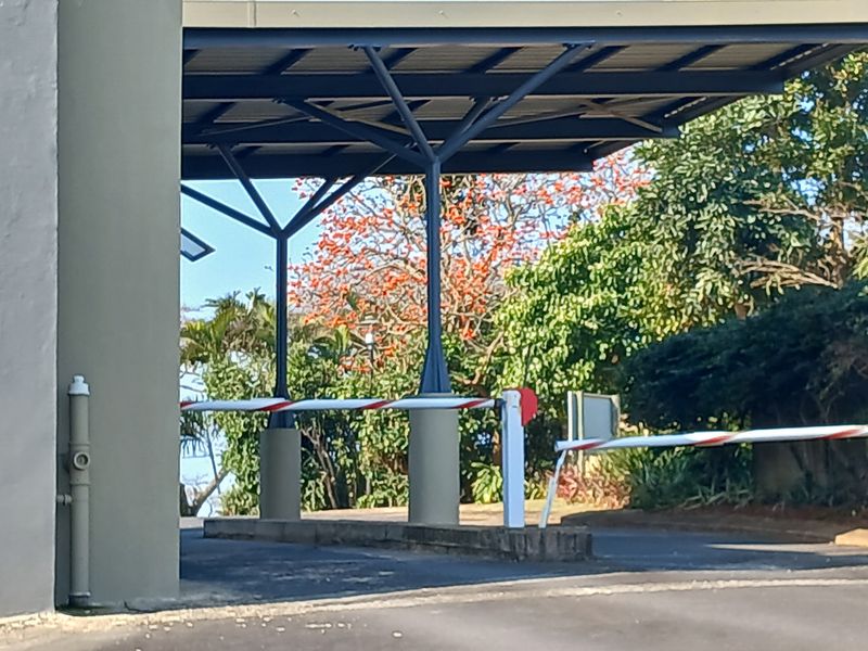 A secure entrance featuring a covered driveway with a functional boom gate system and established landscaping.