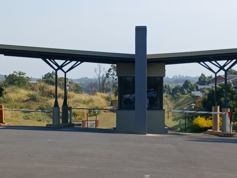 A view of the residential estate security gatehouse featuring a structural steel canopy, boom gate access, and paved driveway entrance.