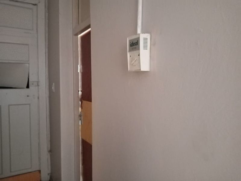 A view of a hallway featuring a wall-mounted thermostat and a vintage panelled door showing signs of wear.