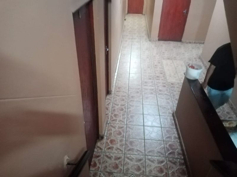 A narrow interior hallway featuring tiled flooring and multiple wooden doors, showing signs of wear and requiring cosmetic updates.