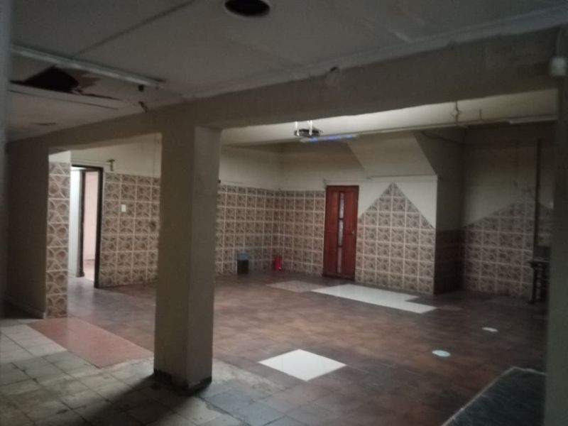 An expansive, open-plan interior space featuring tiled flooring and wall accents, currently vacant and requiring significant renovation to restore its condition.