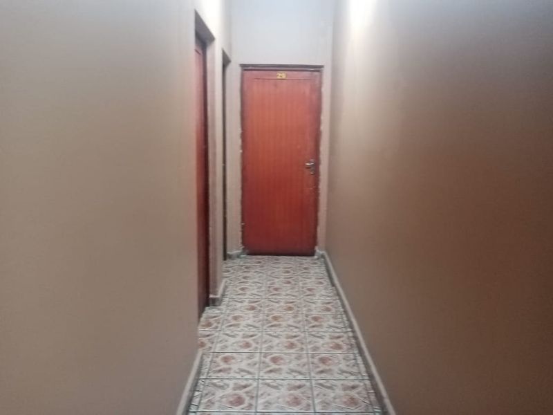 A narrow interior hallway featuring tiled flooring and multiple wooden doors, showing signs of wear on the wall surfaces.