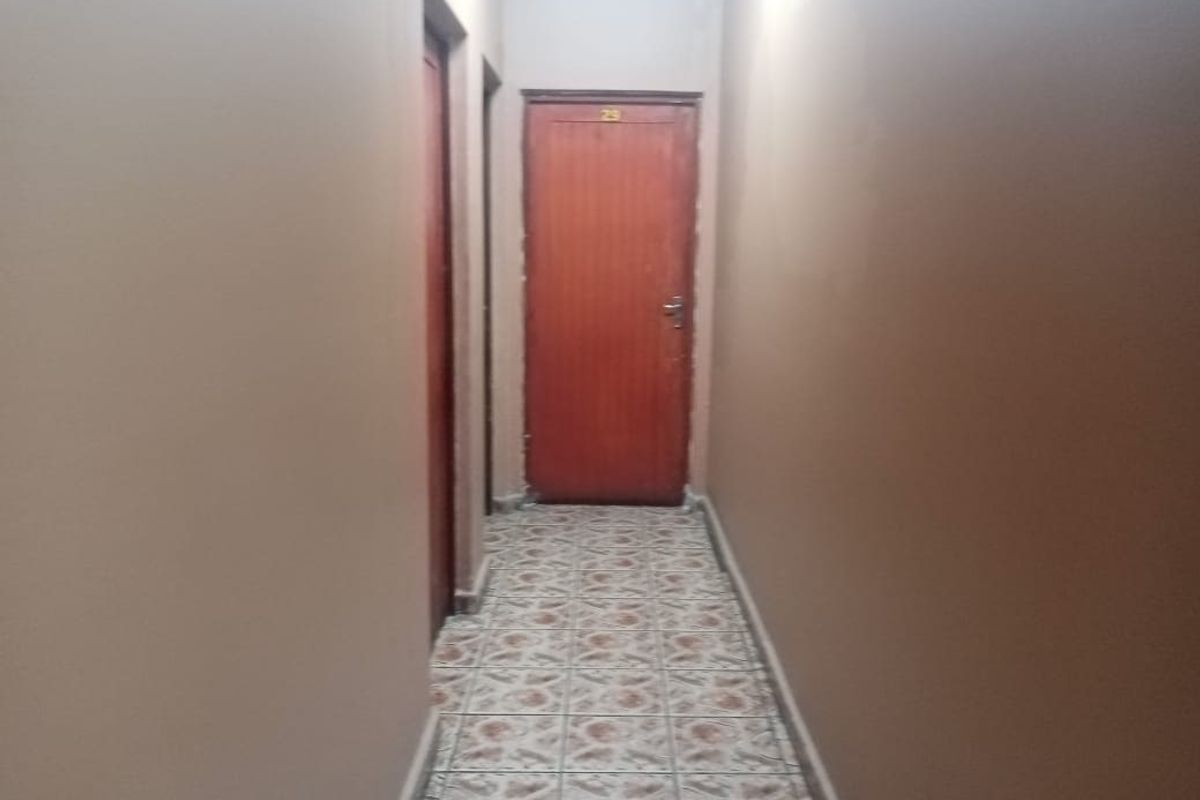A narrow interior hallway featuring tiled flooring and multiple wooden doors, showing signs of wear on the wall surfaces.