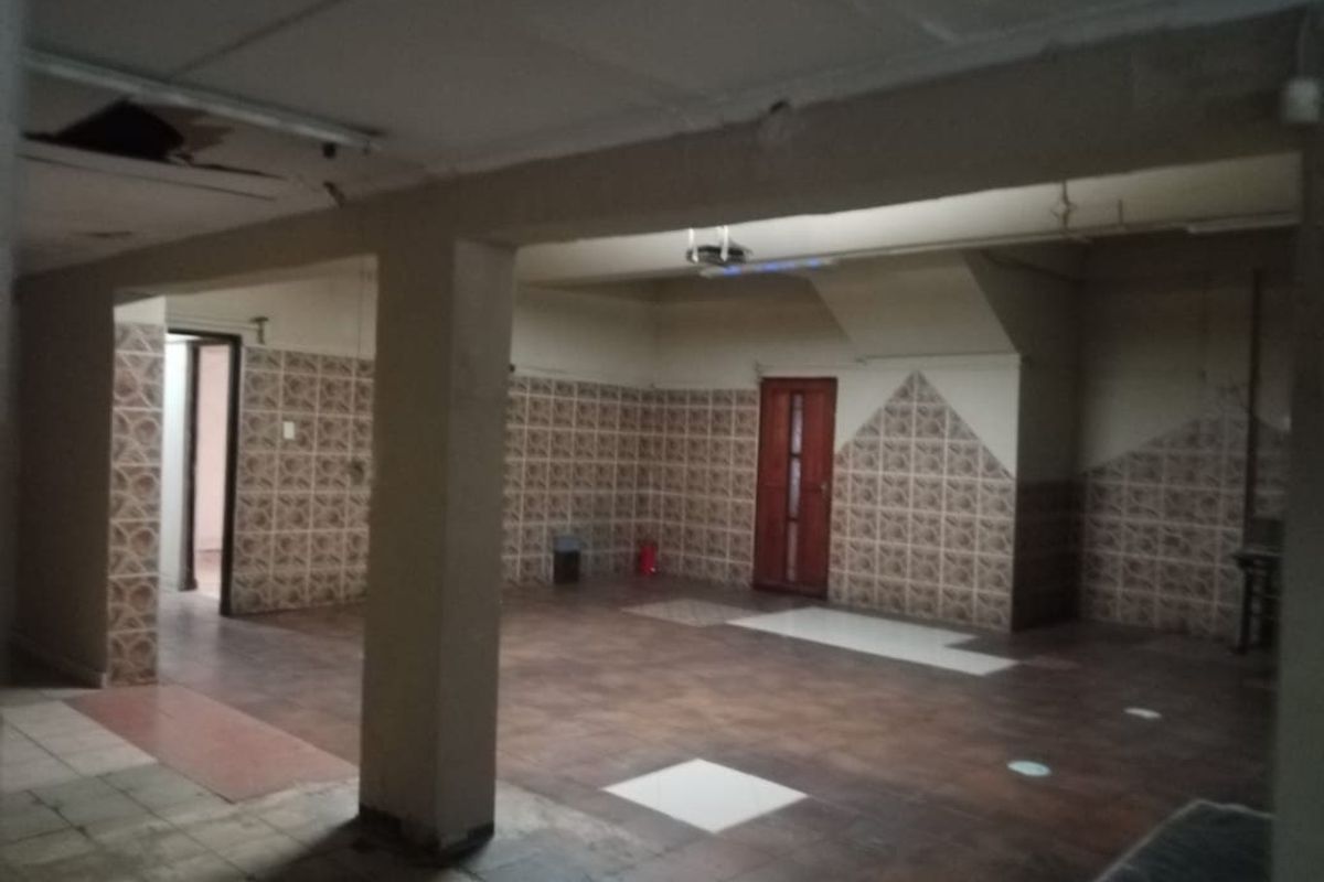 An expansive, open-plan interior space featuring tiled flooring and wall accents, currently vacant and requiring significant renovation to restore its condition.