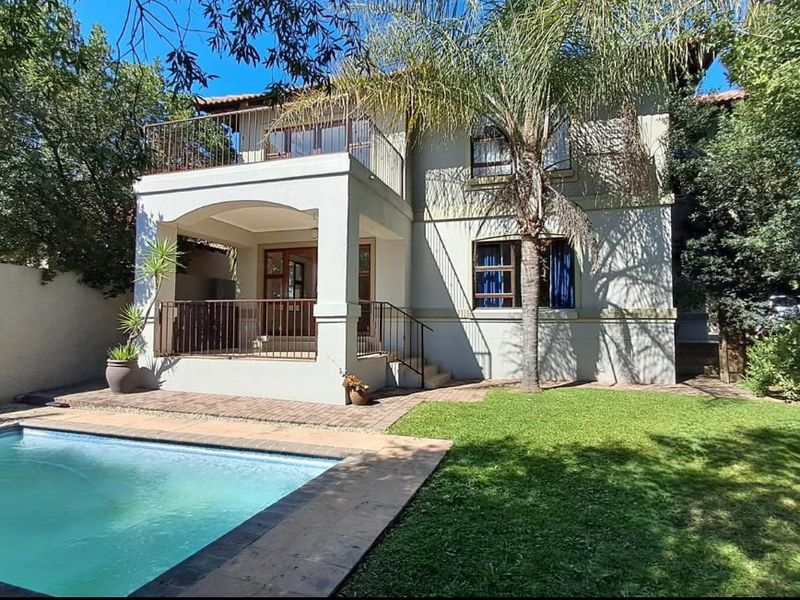 Rear view of a two-story house featuring a swimming pool, paved patio area, and an upper-level balcony with metal railings.