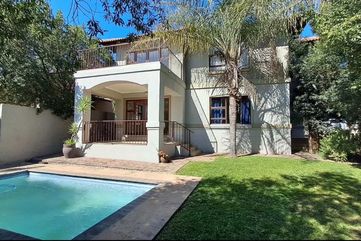 Rear view of a two-story house featuring a swimming pool, paved patio area, and an upper-level balcony with metal railings.