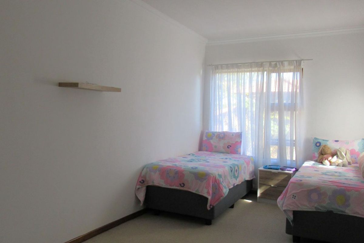 A functional bedroom featuring neutral carpeted flooring, a floating wall shelf, and a window fitted with a curtain rod.