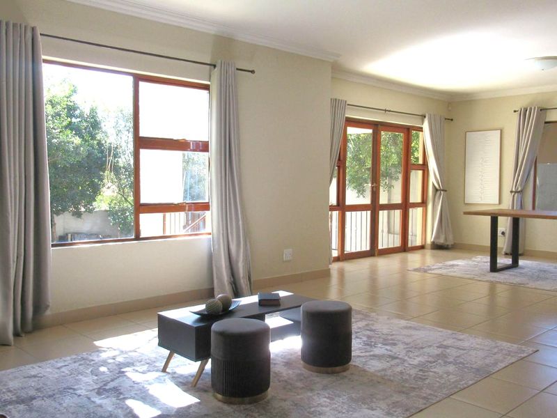 Spacious living area featuring neutral tiled flooring, large wooden-framed windows, and glass-paneled doors providing natural light and garden access.