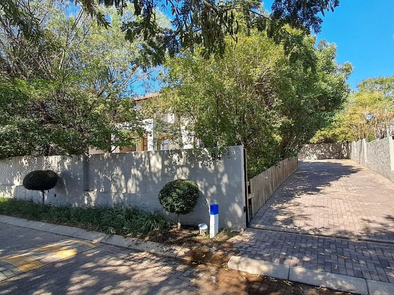 Front view of the property featuring a paved driveway, secure boundary wall, and established garden greenery leading to the entrance.