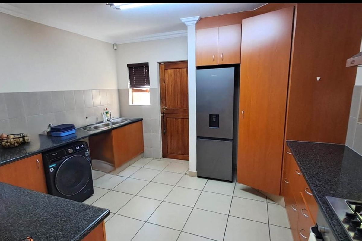Functional kitchen featuring wood-finish cabinetry, granite countertops, tiled backsplash, and integrated gas hob with extractor fan.