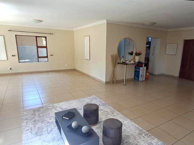 Spacious open-plan living area featuring neutral tiled flooring, clean wall finishes, and natural light through aluminium-framed windows.