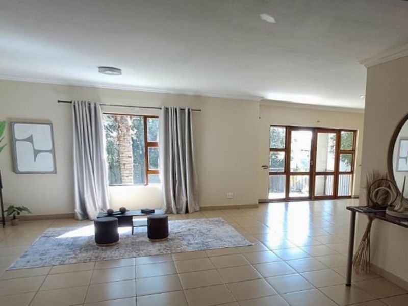 Spacious living area featuring neutral tiled flooring, large windows, and sliding glass doors providing natural light and access to the exterior.