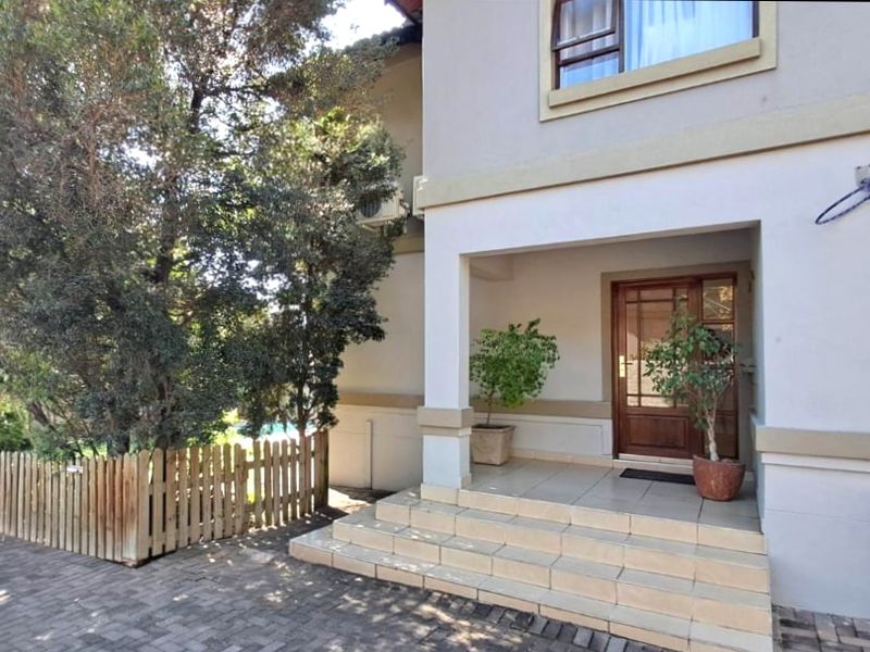 Front entrance of the house featuring tiled steps, a timber front door, and a paved driveway area with established trees.