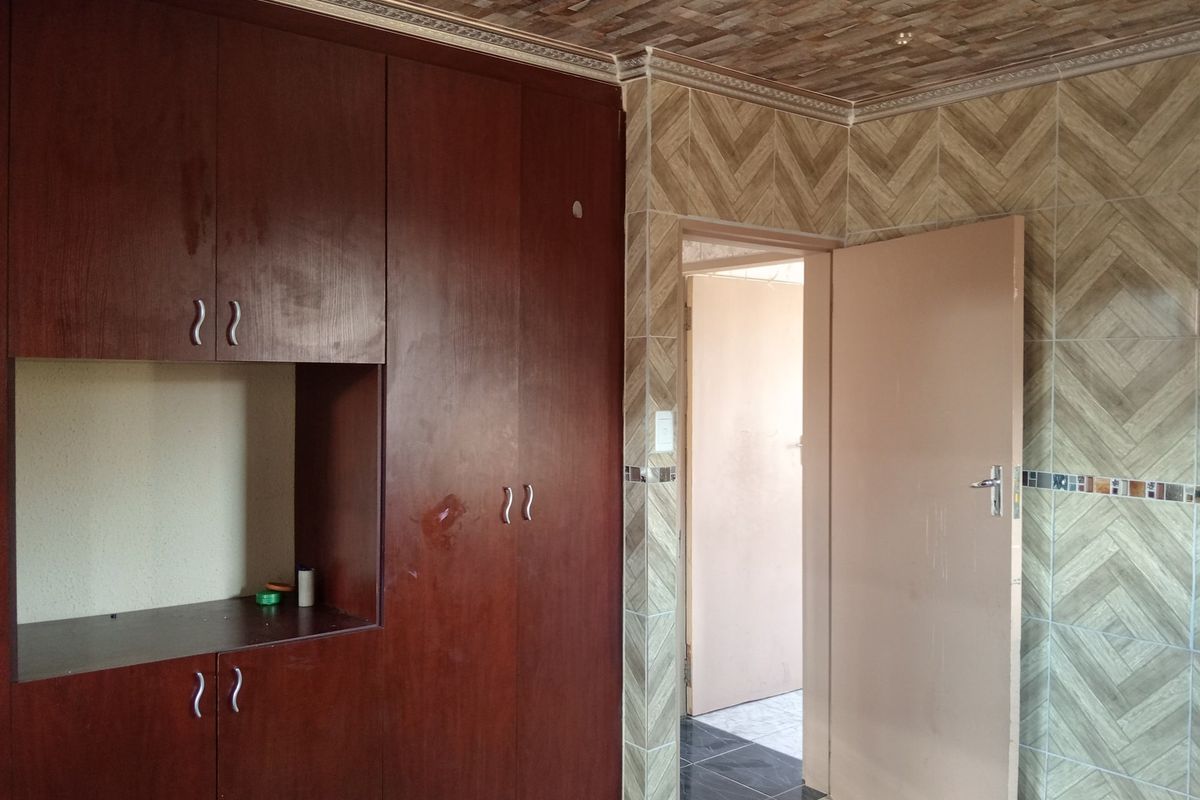 Bedroom featuring built-in wooden cupboards and distinctive tiled wall and ceiling finishes, offering a blank canvas for renovation.