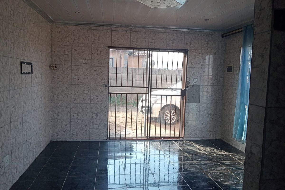 An empty living area featuring fully tiled walls, dark floor tiles, and a secure sliding door entrance with integrated security gate.