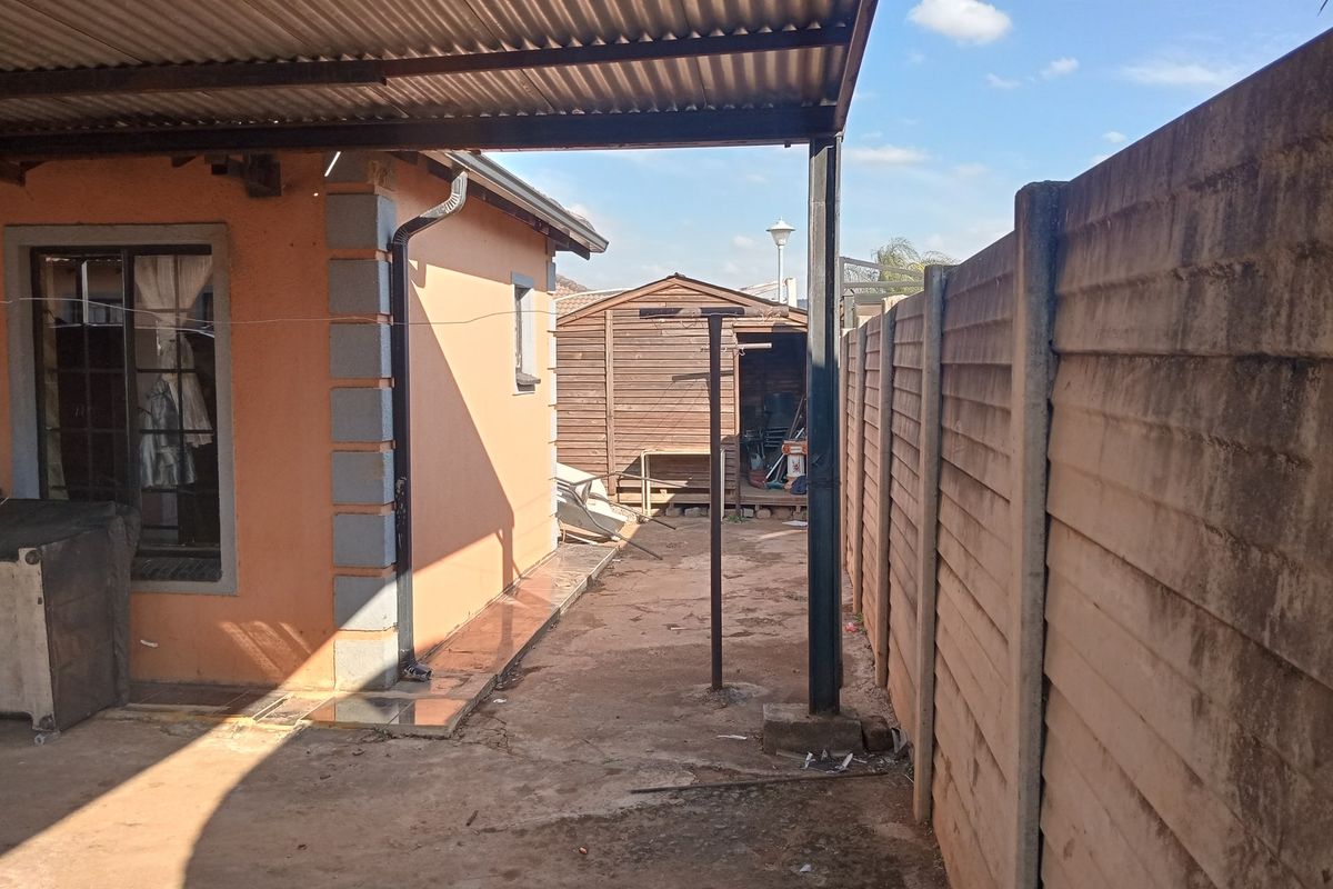 Rear exterior area featuring a covered patio space, concrete paving, and a detached timber storage shed enclosed by a precast concrete boundary wall.