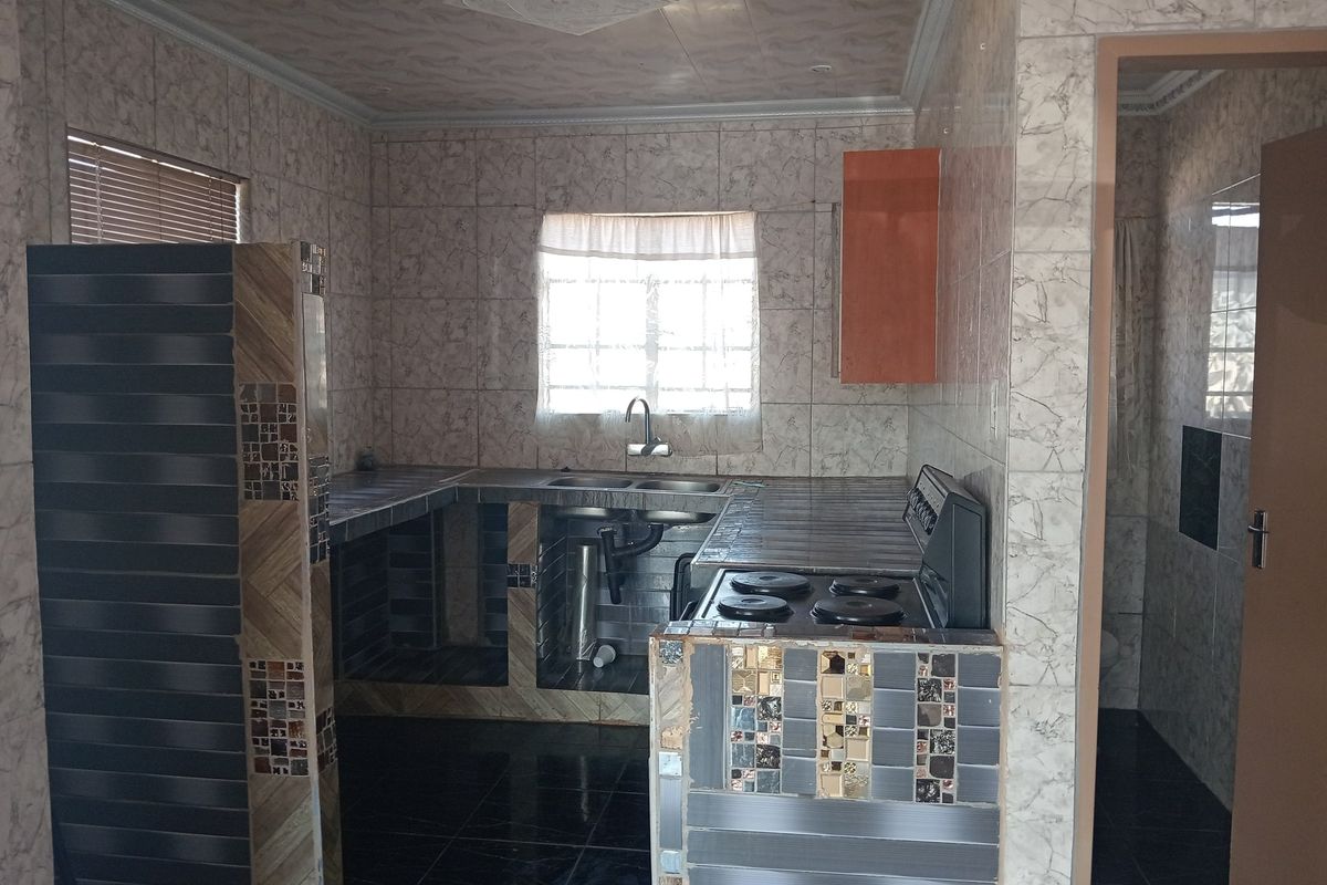 A functional kitchen space featuring tiled countertops, built-in stove, and stainless steel sink, requiring cosmetic updates to improve the overall finish and aesthetic appeal.