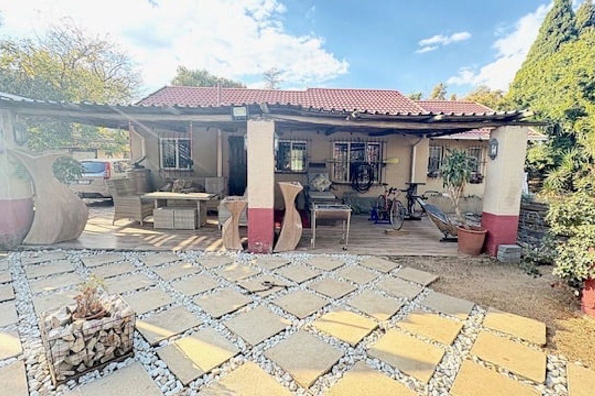 Rear exterior view featuring a covered patio area with paved garden space and established landscaping.