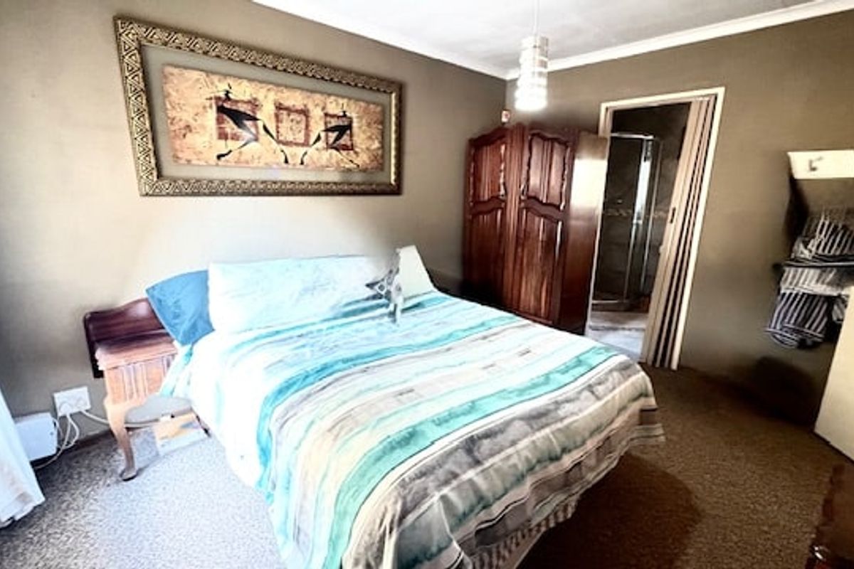 A bedroom featuring carpeted flooring, a central pendant light, and a folding door leading to an en-suite bathroom.