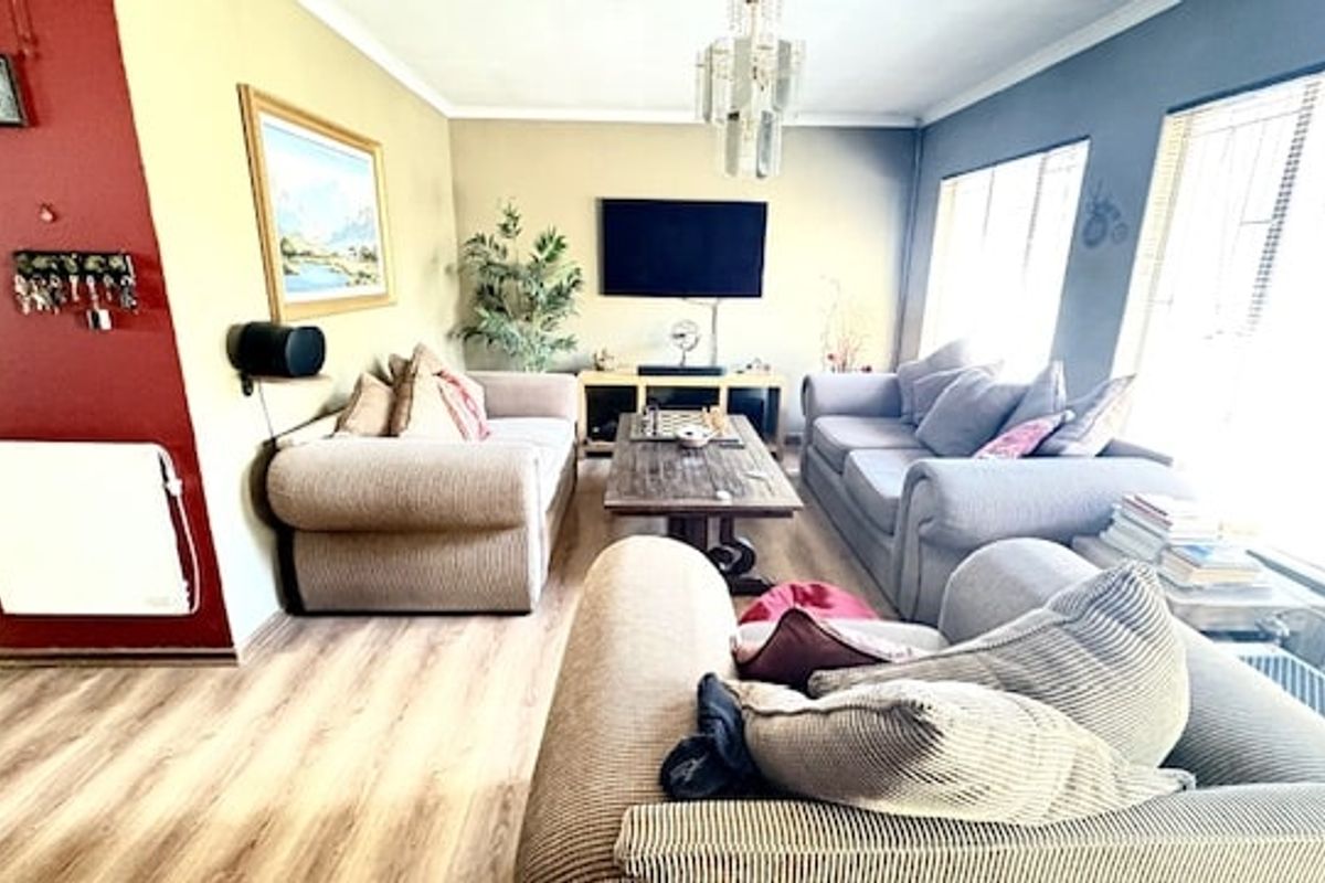 A comfortable living room featuring laminate flooring, large windows with security bars, and a central ceiling light fixture.