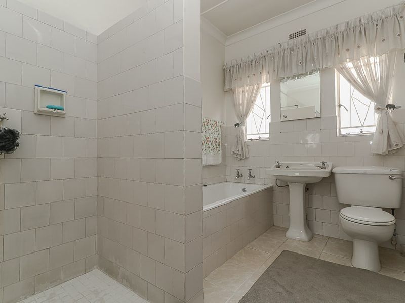 A functional bathroom featuring a tiled shower enclosure, built-in bathtub, pedestal washbasin, and toilet with classic wall tiling.