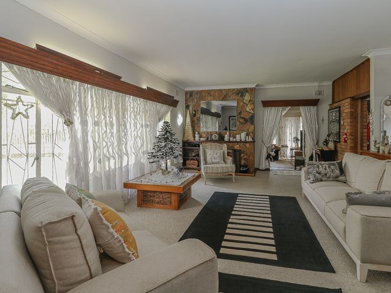 Spacious living room featuring a prominent stone fireplace, brick feature wall, and large windows with timber pelmets, offering a warm and traditional aesthetic.