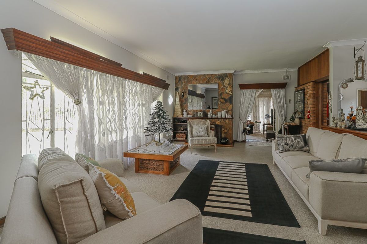 Spacious living room featuring a prominent stone fireplace, brick feature wall, and large windows with timber pelmets, offering a warm and traditional aesthetic.