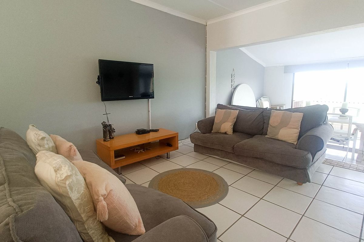 A living room area featuring tiled flooring and a wall-mounted television setup, with an open-plan flow leading to an adjacent space.