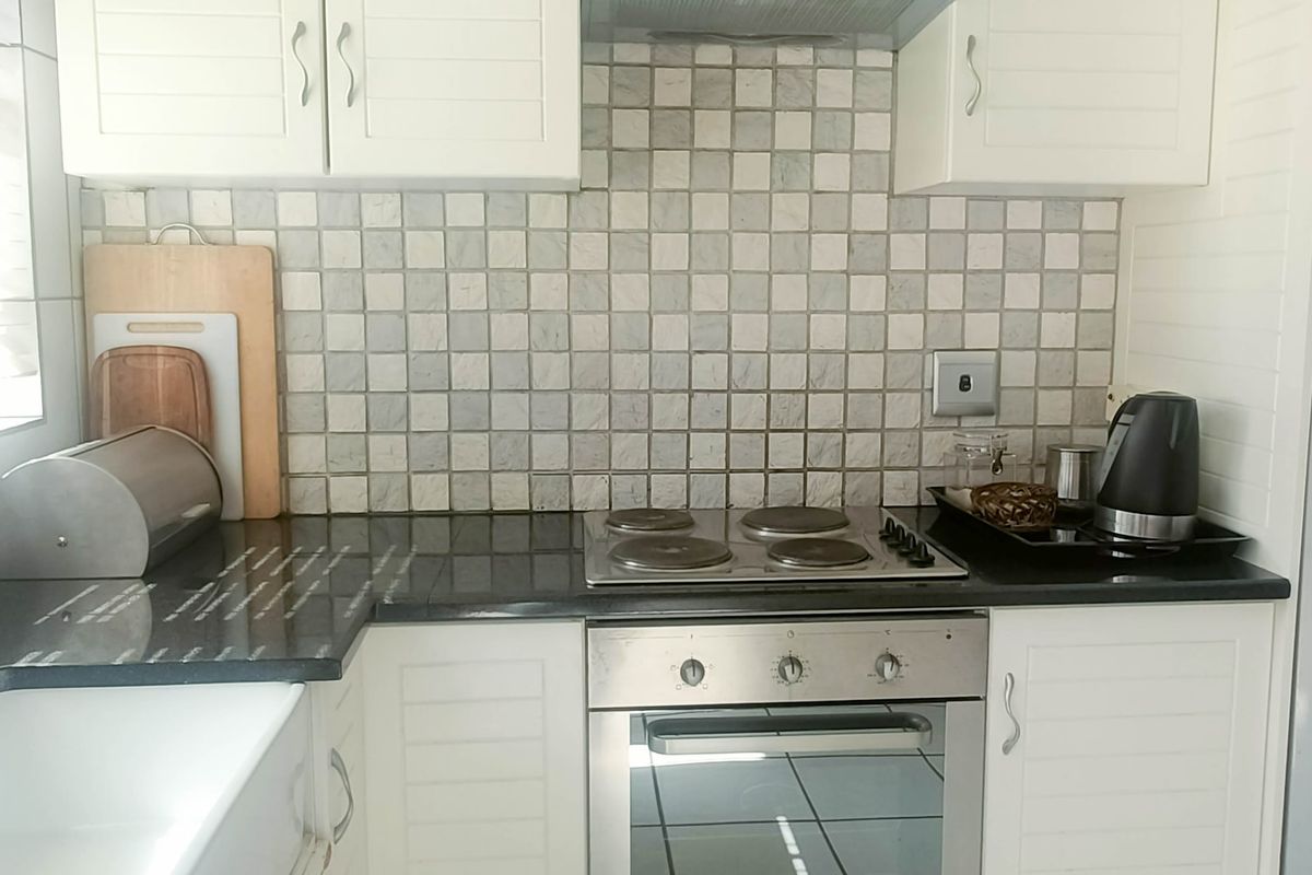 A functional kitchen featuring white cabinetry, dark stone countertops, a built-in electric hob and oven, and a decorative tiled backsplash.