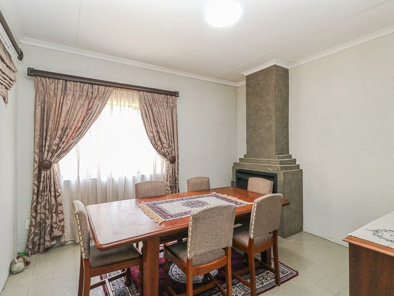 A dining room featuring a built-in fireplace with a textured chimney breast, tiled flooring, and large windows with curtain treatments.