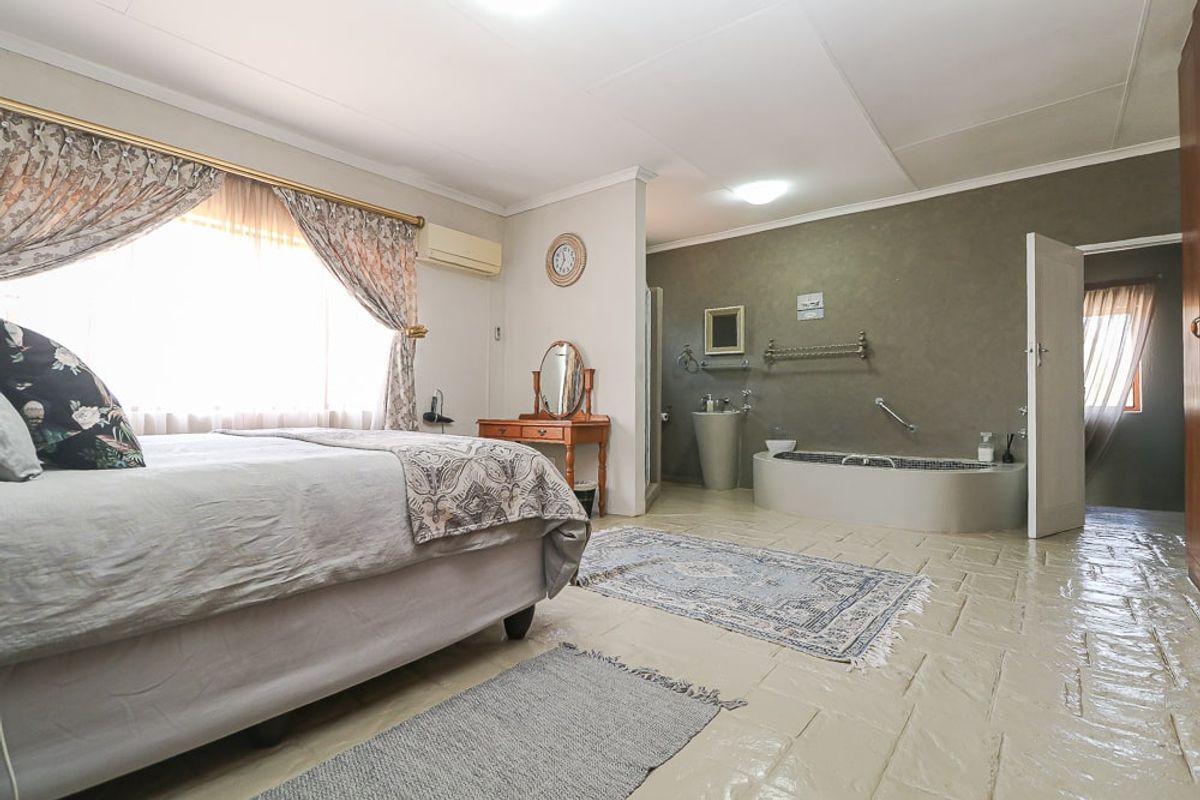 Spacious bedroom featuring an integrated open-plan bathroom with a built-in soaking tub and pedestal basin, finished with tiled flooring.