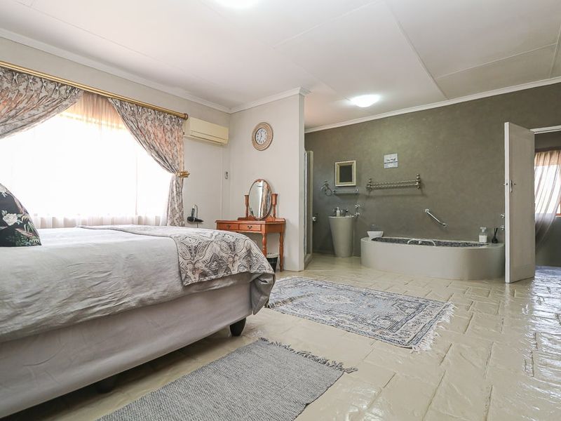 Spacious bedroom featuring an integrated open-plan bathroom with a built-in soaking tub and pedestal basin, finished with tiled flooring.