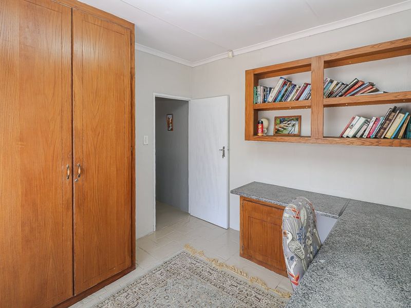A functional home office or study featuring built-in wooden cabinetry, integrated shelving, and a stone-topped desk area.