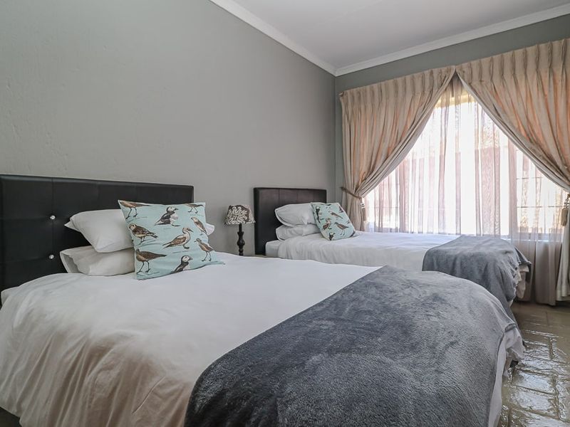 A bedroom featuring tiled flooring, neutral wall finishes, and large windows with curtain treatments, providing a functional and comfortable sleeping space.