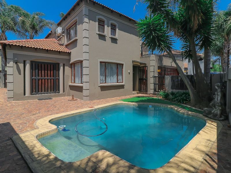 Rear view of the property featuring a private swimming pool, paved patio area, and established garden surroundings.