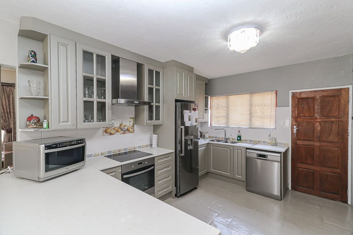 A functional kitchen featuring grey cabinetry, stone-look countertops, stainless steel appliances, a built-in oven, and a glass-fronted display cabinet.