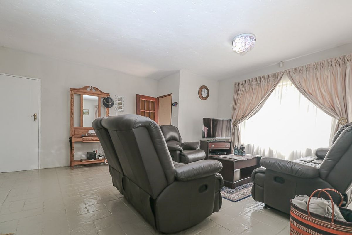 A living room featuring tiled flooring, a central ceiling light fixture, and a large window with curtains.
