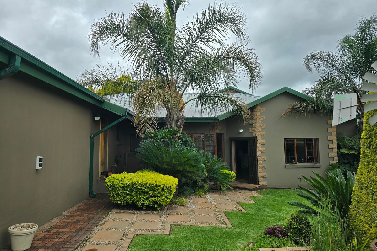 A well-maintained rear exterior view featuring stone-clad accents, brick pathways, and a lush landscaped garden area.