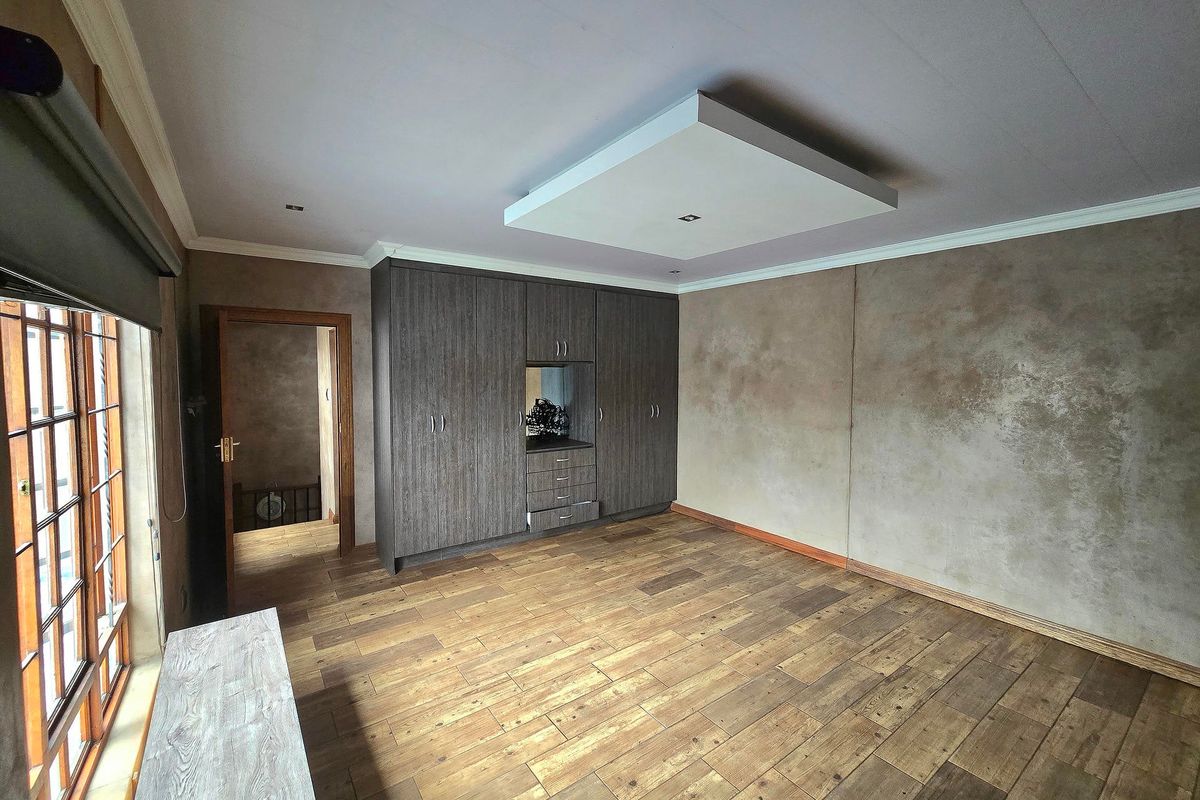Spacious bedroom featuring built-in cupboards, timber-look floor tiles, and a modern recessed ceiling detail, offering a clean and neutral canvas.