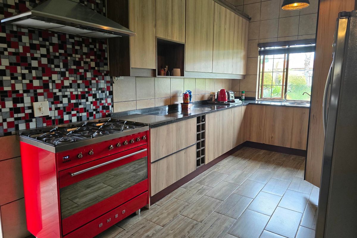 A functional kitchen featuring wood-look cabinetry, granite countertops, a striking red Smeg gas stove, and a mosaic tile backsplash.